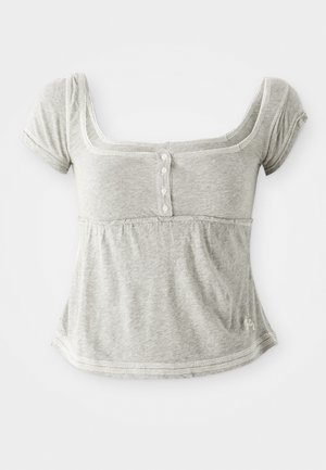Haut gris à manches courtes en coton doux avec un col rond, doté d'un plastron à boutons et de surpiqûres décoratives le long des bords.