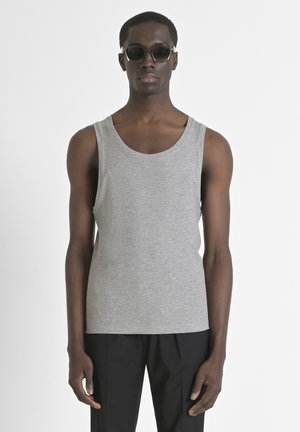 Débardeur gris à côtes avec de larges ouvertures au niveau des bras, encolure ronde et silhouette ajustée, accompagné de pantalons noirs et de lunettes de soleil.