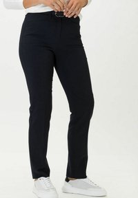 Pantaloni blu navy dal design elegante e dritto, con passanti per cintura e una vita liscia, abbinati a scarpe da ginnastica bianche.
