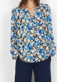 Blommig blus med svart bakgrund prydd med blå, gröna och beige blommor. Lättviktig tyg med v-ringning och långa, puffiga ärmar.