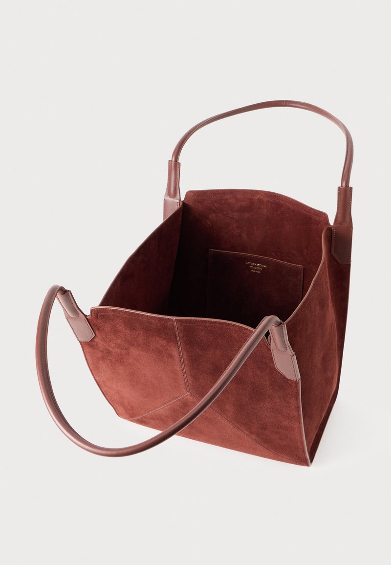 Sac fourre-tout en daim marron foncé ouvert avec deux poignées en cuir arrondies et une poche intérieure avec un texte logo doré.