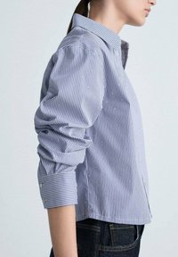 Striped button-up shirt in blue and white, featuring pearl accents, long sleeves with cuffs, and a classic collar. Smooth fabric texture.