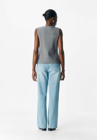 Top gris sans manches avec une texture lisse, associé à un jean large bleu clair, vue de dos sur fond blanc.