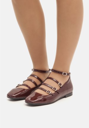 Ballerine in pelle verniciata bordeaux con più fasce sottili e fibbie regolabili. Caratterizzate da una punta arrotondata e una suola piatta. Texture liscia e lucida.