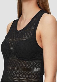 Musta toppi, jossa on kohokuvioitu timantinmuotoinen kuvio ja hihaton malli. Pyöreä pääntie ja resorireunus reunoilla.