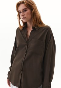 Camicia a maniche lunghe verde oliva scuro realizzata in un morbido tessuto testurizzato. Presenta una chiusura con bottoni sul davanti e una tasca sul petto sinistro.