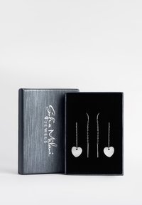 Silberne herzförmige Ohrringe in einer Geschenkbox mit glatter Oberfläche, hängenden Ketten und einem strukturierten schwarzen Innenraum. Die Box hat eine metallische Außenseite.