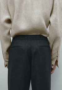 Beige linen shirt with button accents, paired with dark gray pants featuring an elastic waistband and back pockets.