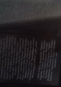 Étiquette en tissu noir avec texte blanc, affichant les instructions d'entretien et les matériaux, y compris "100 % coton" en plusieurs langues.