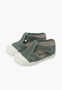 Grüne Segeltuchschuhe mit einer weißen Gummizahlkappe, die über Kreuzriemen und ein offenes Design verfügen, bieten Atemfähigkeit und Komfort.