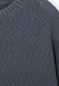 Gros plan d’un tissu de pull tricoté gris foncé avec col côtelé visible et motif de points texturé.