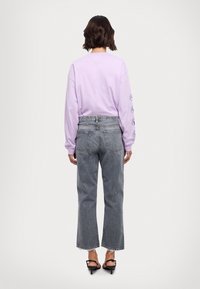 Camiseta de manga larga color lavanda con diseños impresos en las mangas, combinada con jeans de mezclilla gris claro con dobladillos deshilachados y un ajuste relajado.