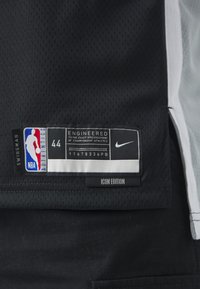 Juodas NBA marškinėlis su tinkliniu tekstūru. Yra Nike prekės ženklas ir daugiaspalvis logotipas. Įtraukti etiketės su dydžiu 44, "Swingman" ir "Icon Edition".