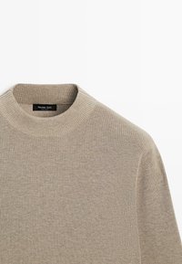 Beiger Strickpullover mit Rundhalsausschnitt, gerippter Struktur und eng anliegenden Ärmeln. Mit einem Etikett mit der Aufschrift "Massimo Dutti".