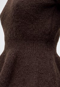 Gros plan d'un tissu tricoté marron avec des motifs de points variés et un détail de ceinture côtelée.