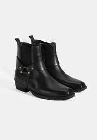 Bottines en cuir noir avec un bout rond, des panneaux latéraux élastiques et une sangle décorative avec des accents dorés ; talon bas carré.