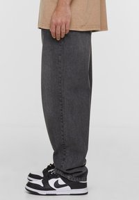 Pantalones de mezclilla gris con un corte holgado, con pierna recta y una textura sutil, combinados con zapatillas negras y blancas.