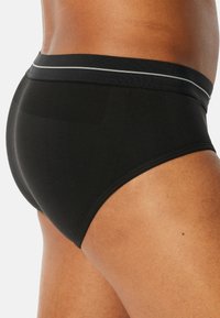 Schwarze Unterhose mit glatter Textur, ausgestattet mit einem grauen Bund und einer figurbetonten Passform, die ihre klaren Linien und das schlichte Design zur Geltung bringt.