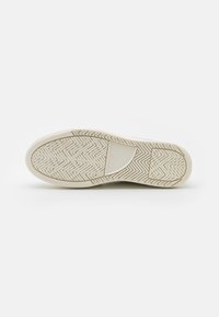 Semelle d'une basket beige clair avec un motif en chevrons et une zone rectangulaire pour le logo au milieu.