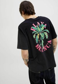 Sort bomulds t-shirt med et levende grønt plante design og pink tekst "Playa Blanca" på ryggen samt en afslappet pasform.