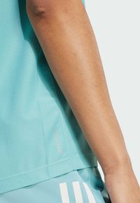 T-shirt de sport bleu clair avec un design en maille texturée, des manches courtes et un petit logo "AEROREADY" sur l'ourlet latéral.