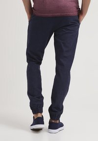 Marine joggers gemaakt van zachte stof met elastische boorden bij de enkels. Gestyled met een relaxte pasvorm en gecombineerd met marine sneakers.