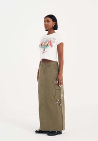 Crop top in het wit met kleurrijke grafische print, gecombineerd met een lange olijfgroene cargorok met zijzakken en geborduurde details.