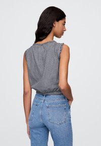 Ermeløs svart-hvitt gingham-topp med volangdetaljer på skuldersømmene, kombinert med lyseblå høytlivsjeans med lommer.