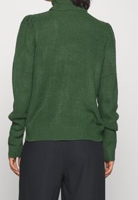 Pull vert en maille avec un col montant, une texture côtelée et des poignets ajustés, avec un détail froncé aux épaules et une coupe décontractée.