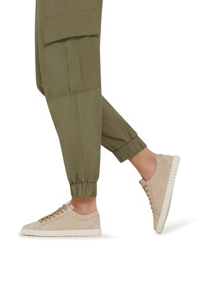 Beige Wildleder-Sneaker mit strukturierten Akzenten und einer weißen Gummisohle, kombiniert mit lockeren olivgrünen Cargo-Hosen mit elastischen Bündchen an den Knöcheln.
