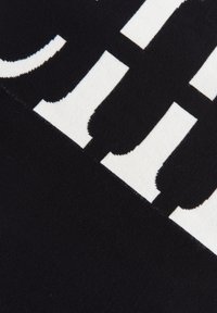 Svart tyg med stora vita bokstäver. Texturen verkar slät, med rena kanter och ett konsekvent mönster. Designen är djärv och grafisk.