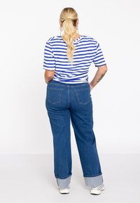 Gestreiftes blau-weißes Kurzarmhemd kombiniert mit hochgeschnittenen, weiten Jeans mit umgekrempelten Säumen. Standard-Gesäßtaschen sichtbar.