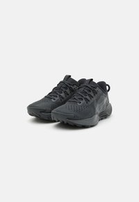 Zwarte sportschoenen met een bovenwerk van gestructureerde stof, versterkte neus en gelaagd ontwerp. Beschikt over een gevoerde kraag en vetersluiting.