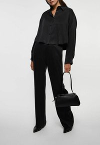 Sort satin cropped skjorte med krave og knaplukning, parret med matchende vide bukser. Accessoriseret med en lille sort håndtaske.