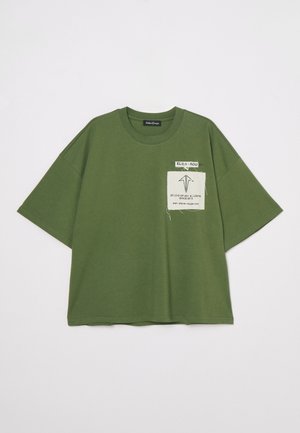 Olive green oversized T-shirt, cotton material, crew neck, short sleeves, featuring a white label with black text on the left side.