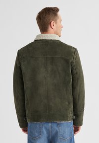 Olivgrüne Wildlederjacke mit Schafslederkragen, geradem Design, Rückennahtdetails und metallischem Verschluss am Saum.
