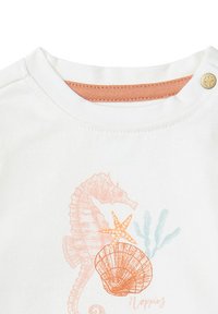 Weißes Baumwoll-T-Shirt mit einem orangefarbenen Seepferdchen, einem Seestern und einem Muschel-Print. Druckknopfverschluss an der Schulter, mit einem hellorangefarbenen Halsausschnitt.