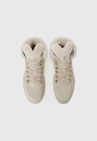 Beige magas szárú sneaker, puha velúrból készült, prémes bélésű gallérral, fémből készült fűzőkkel és fűzőlyukakkal, valamint texturált elülső panelel.