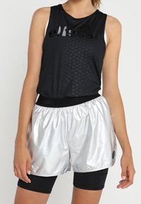 Czarna bezrękawnikowa koszulka sportowa z fakturowanym wzorem, w połączeniu z błyszczącymi srebrnymi szortami z elastycznym pasem i detalem z logo.