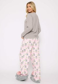 Gray long-sleeve top with round neckline, paired with pink pajama pants featuring a pattern of illustrated raccoons. Gray fuzz slippers.