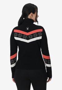 Pull à col roulé noir avec des motifs en zigzag rouges et blancs, des motifs floraux et un petit logo à l'arrière. Matière en maille chaude.