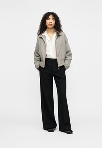 Gray and black checked bomber jacket with a zip front, worn over a white shirt, paired with black wide-leg trousers and glossy shoes.