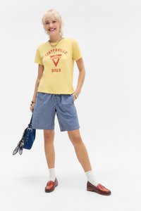 Yellow graphic t-shirt with red text, blue and white checkered shorts, white socks, and brown loafers. Accessories include a blue bag.