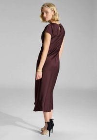 Burgundy midi mekko tasaisesta kankaasta, jossa on hihattomat hihat ja avaus selässä. Yhdistetty mustien nauhakorollisten kenkien ja kultaisien yksityiskohtien kanssa.