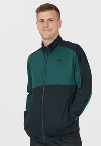 Svart och grön sportjacka med dragkedja fram, med en texturerad övre panel och en solid nedre del. Försedd med FZ-logotypen.