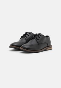 Chaussures noires en cuir avec une pointe arrondie, un laçage, des détails de couture discrets et une semelle crantée marron pour une meilleure adhérence.