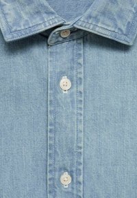 Chemise en denim bleu clair avec un col pointu, une fermeture à boutons sur le devant et des boutons blancs. Caractérisée par une texture lisse et des coutures régulières.