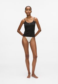 Melnā piegulošā korsetē ar šaurām siksnām, priekšpusē ar nelielu baltu logo, apvienota ar gaišas krāsas peldbiksēm.