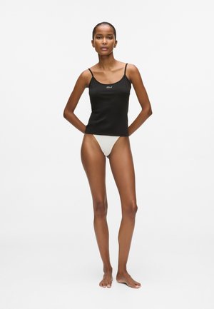 Melnā piegulošā korsetē ar šaurām siksnām, priekšpusē ar nelielu baltu logo, apvienota ar gaišas krāsas peldbiksēm.