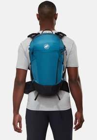 Teal vandringsryggsäck med svart bas, vadderade remmar och extern förvaring. Har logotyp på framsidan och justerbara stängningsdetaljer.